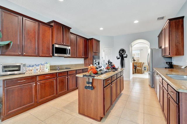 kitchen featuring a kitchen island, sink, light stone countertops, light tile patterned floors, and appliances with stainless steel finishes