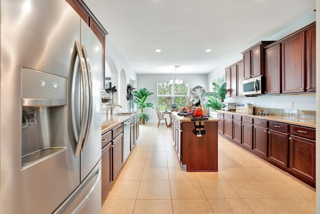 kitchen featuring light stone countertops, sink, a kitchen island, hanging light fixtures, and stainless steel refrigerator with ice dispenser