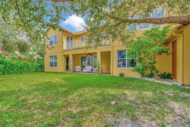 rear view of property with a balcony, a patio, a lawn, and ceiling fan