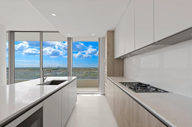 kitchen with sink, stainless steel gas cooktop, tasteful backsplash, a water view, and white cabinets