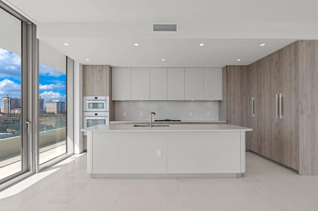 kitchen featuring white cabinets, floor to ceiling windows, sink, and an island with sink