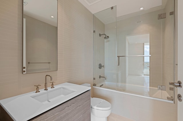 full bathroom featuring shower / bath combination with glass door, vanity, tile walls, and toilet