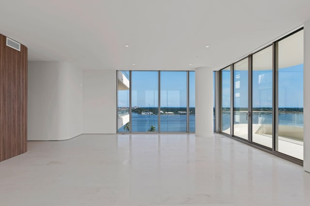 unfurnished room featuring a healthy amount of sunlight, a water view, and a wall of windows