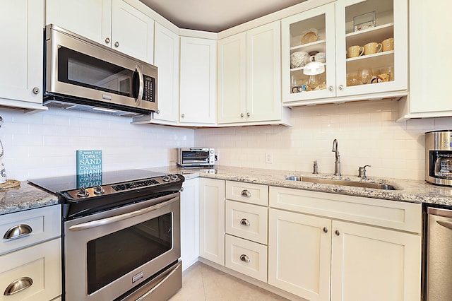 kitchen featuring light stone counters, tasteful backsplash, appliances with stainless steel finishes, glass insert cabinets, and a sink