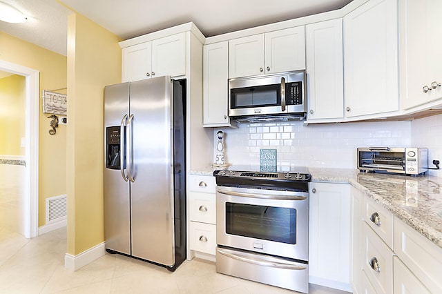 kitchen featuring a toaster, light tile patterned floors, appliances with stainless steel finishes, white cabinetry, and light stone countertops