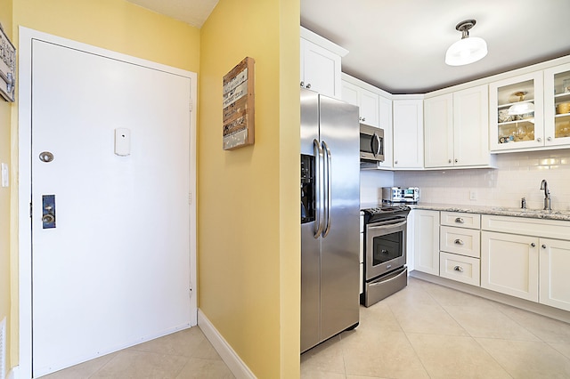 kitchen with light tile patterned floors, white cabinets, decorative backsplash, appliances with stainless steel finishes, and a sink