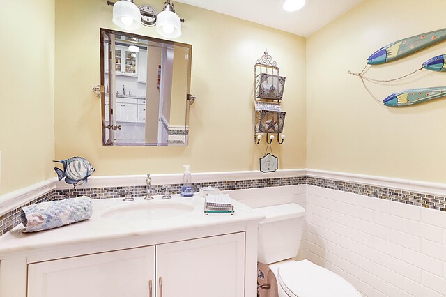 bathroom with toilet, wainscoting, vanity, and tile walls