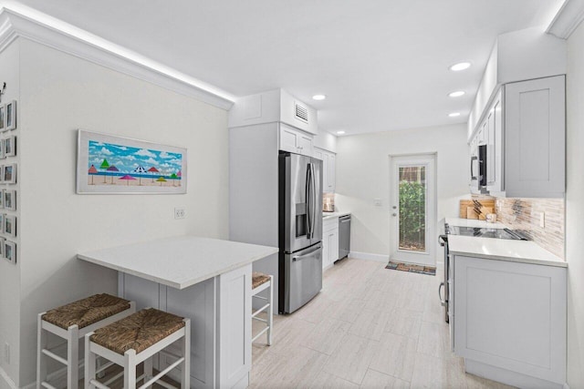 kitchen featuring a kitchen bar, kitchen peninsula, white cabinetry, stainless steel appliances, and decorative backsplash