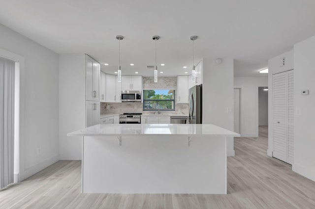 kitchen featuring white cabinets, stainless steel appliances, decorative light fixtures, and a kitchen island