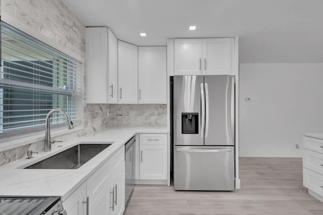 kitchen with appliances with stainless steel finishes, white cabinets, sink, and light stone counters