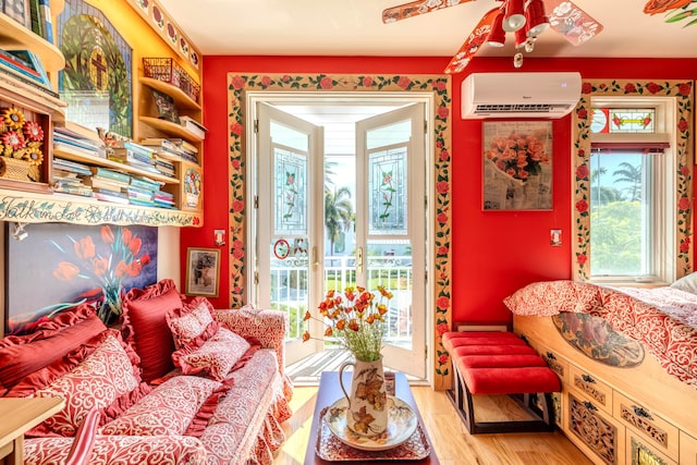 sitting room with light wood-type flooring, a wall unit AC, ceiling fan, and plenty of natural light