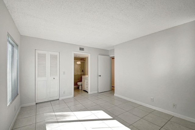 unfurnished bedroom with a textured ceiling, ensuite bathroom, a closet, and light tile patterned floors