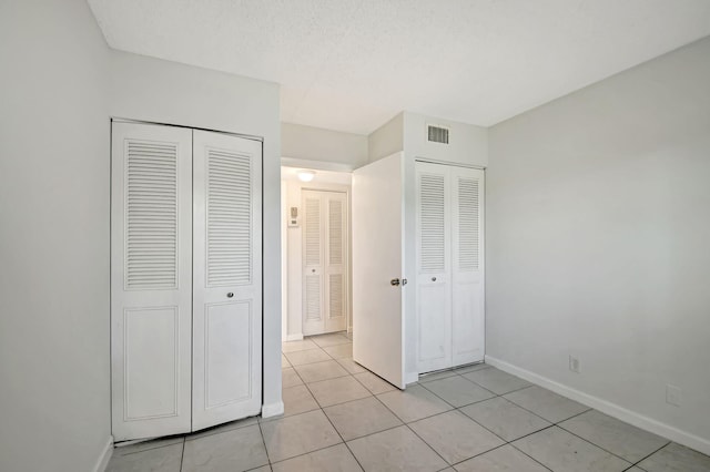 unfurnished bedroom featuring two closets, a textured ceiling, and light tile patterned floors