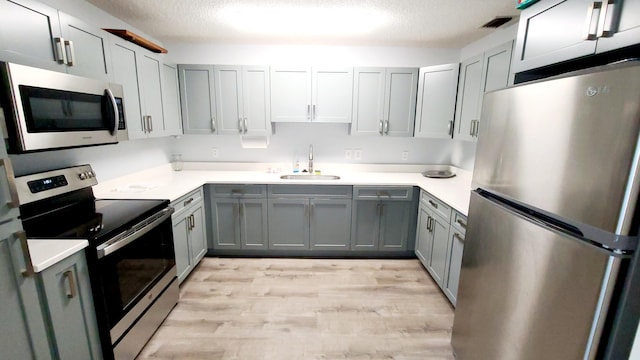 kitchen with appliances with stainless steel finishes, light hardwood / wood-style flooring, a textured ceiling, and sink