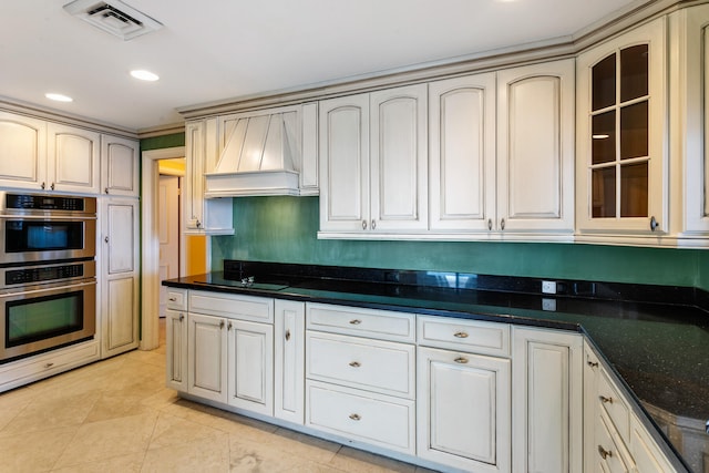 kitchen with double oven, cream cabinets, dark stone counters, black electric stovetop, and custom exhaust hood