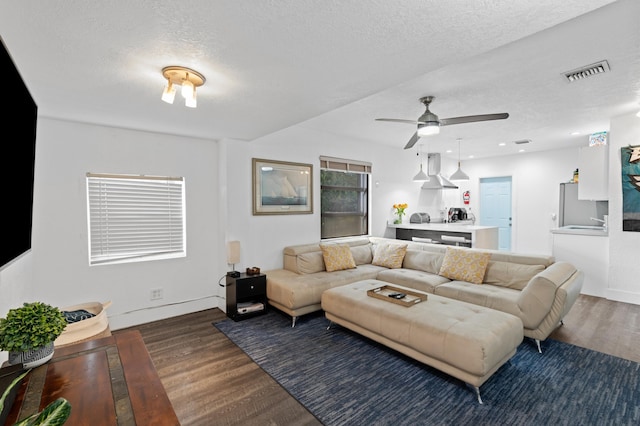 living room featuring dark wood-type flooring, ceiling fan, and a textured ceiling