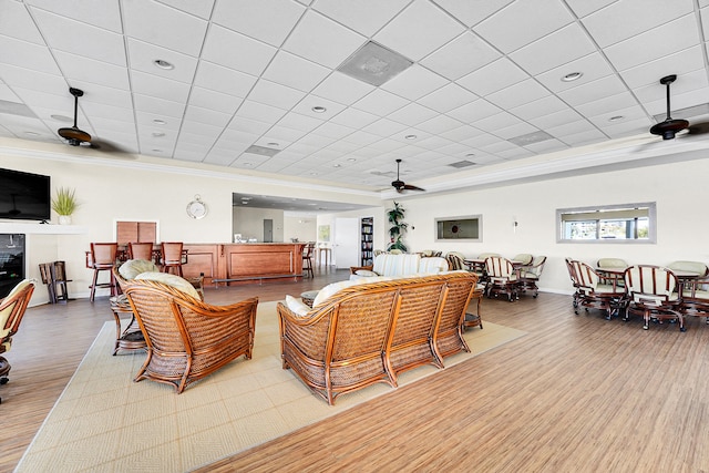 living room with ceiling fan, a drop ceiling, wood-type flooring, and ornamental molding