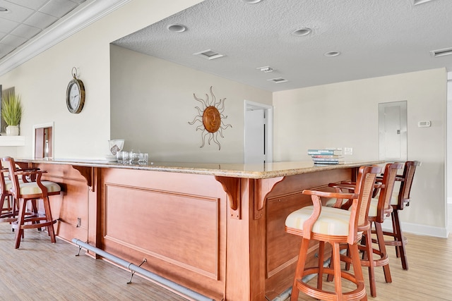 bar featuring crown molding, light hardwood / wood-style flooring, and a textured ceiling