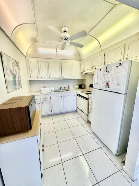 kitchen with white appliances, light tile patterned flooring, sink, ceiling fan, and white cabinets