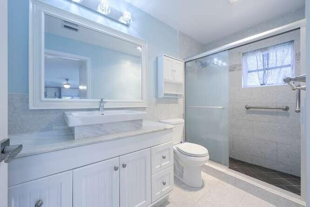 bathroom featuring tile patterned floors, toilet, vanity, tile walls, and an enclosed shower