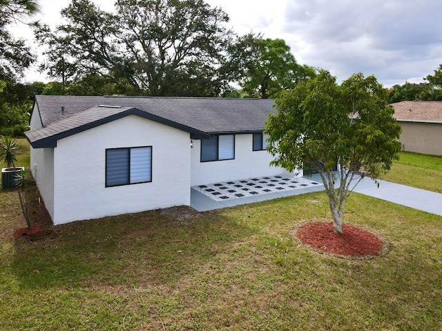 view of front facade featuring central air condition unit, stucco siding, roof with shingles, and a front yard