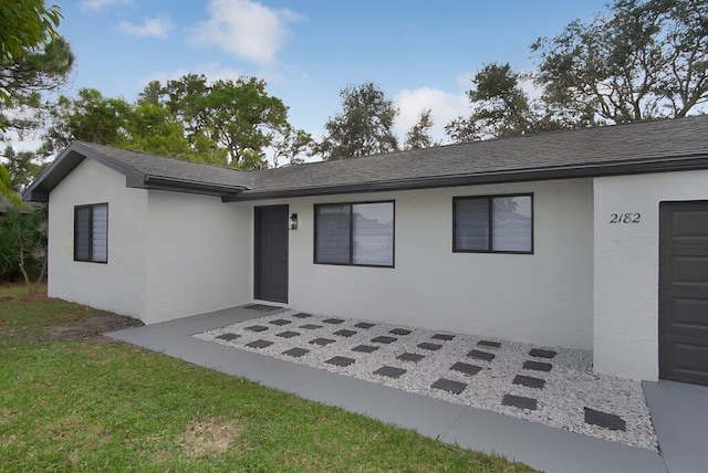 ranch-style house with roof with shingles, a front yard, and stucco siding