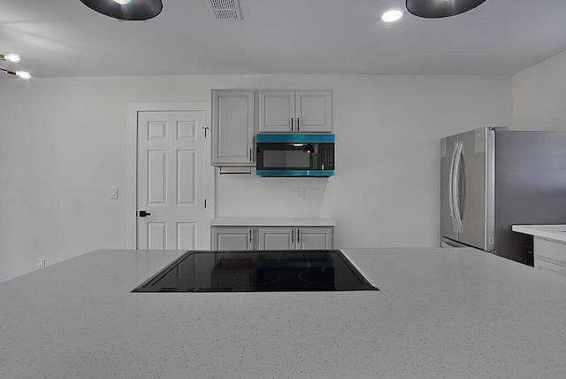 kitchen with black electric stovetop, light countertops, visible vents, freestanding refrigerator, and white cabinets