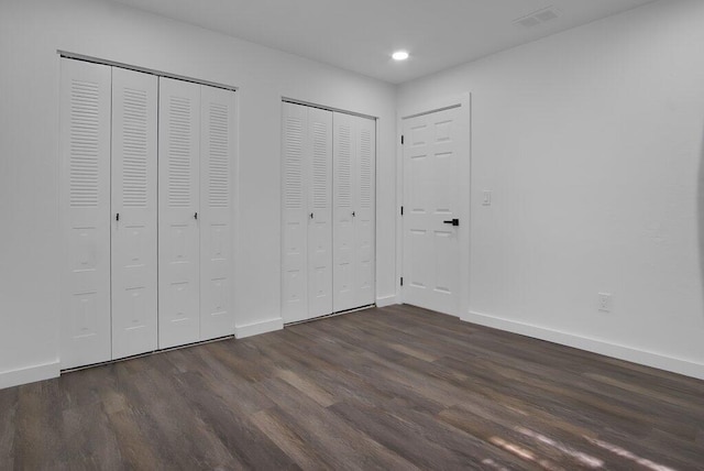 unfurnished bedroom with dark wood-style floors, baseboards, and two closets