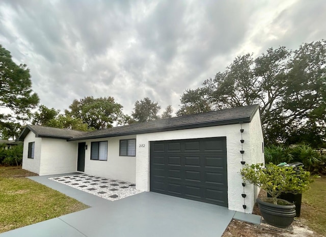 ranch-style house with a garage, driveway, a shingled roof, and stucco siding