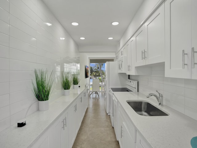 kitchen with white appliances, tasteful backsplash, light stone countertops, sink, and white cabinets