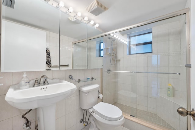 bathroom with toilet, backsplash, tile walls, and a shower with door