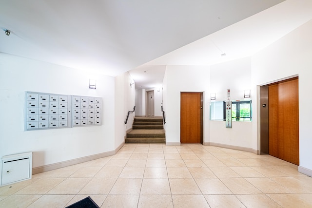 empty room with elevator, light tile patterned flooring, and a mail area