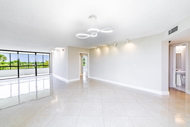 tiled empty room featuring a wealth of natural light, a chandelier, a textured ceiling, and rail lighting