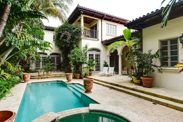 back of property featuring a pool with hot tub, a balcony, a patio, and french doors