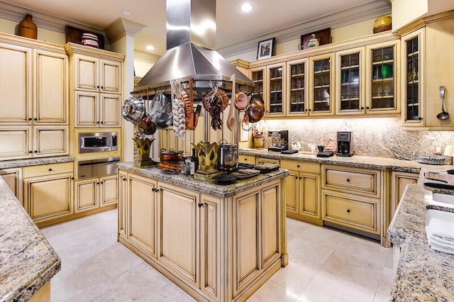 kitchen with light stone counters, stainless steel microwave, a center island, island exhaust hood, and backsplash