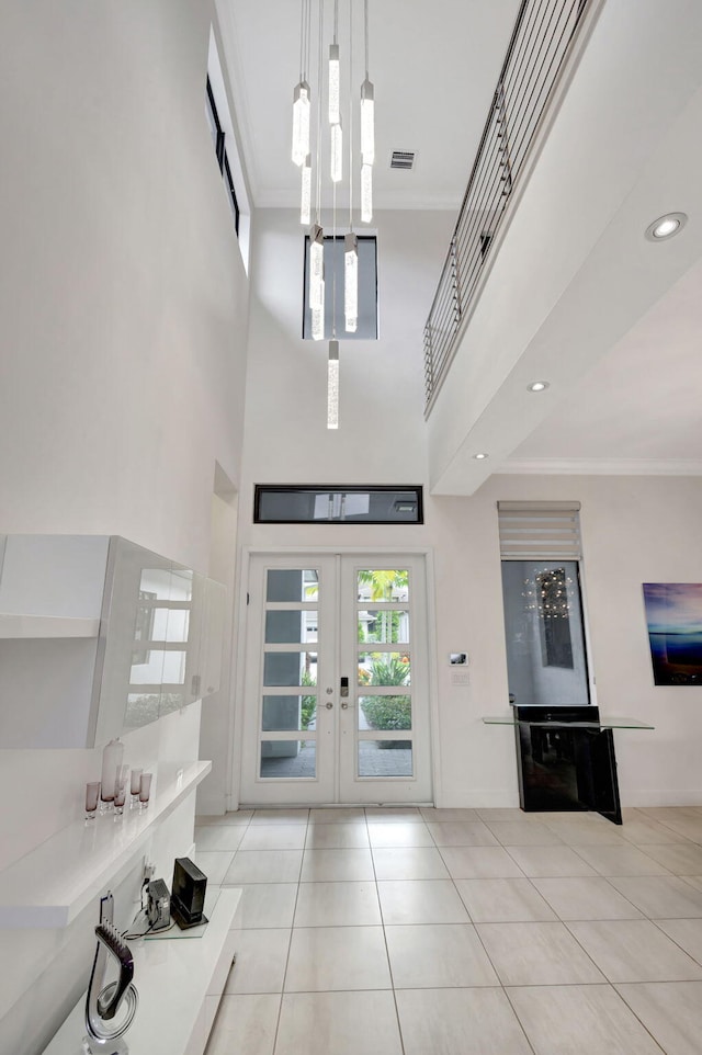 tiled entrance foyer with french doors, a towering ceiling, and ornamental molding