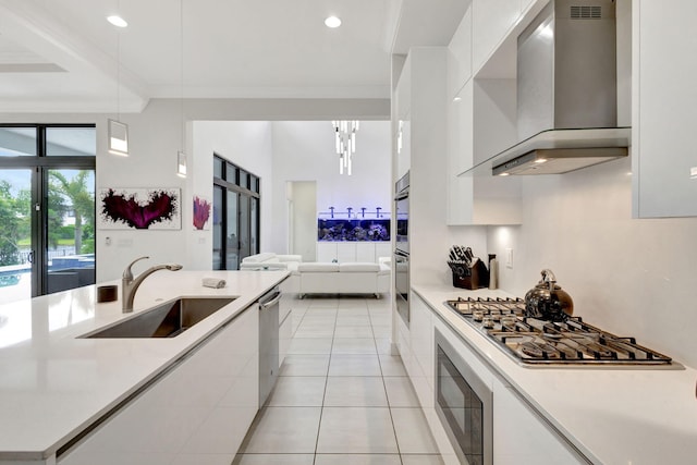 kitchen with appliances with stainless steel finishes, sink, white cabinetry, and wall chimney range hood