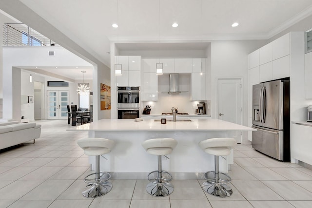 kitchen featuring appliances with stainless steel finishes, white cabinetry, a kitchen breakfast bar, and wall chimney range hood