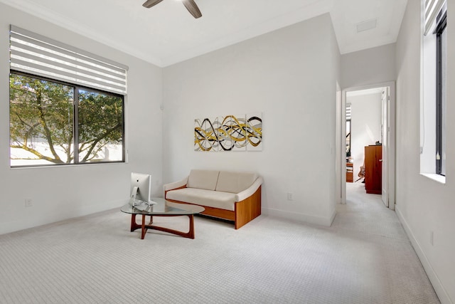 living area with ceiling fan, light colored carpet, and ornamental molding