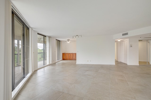 tiled empty room with ceiling fan, track lighting, and a wall of windows