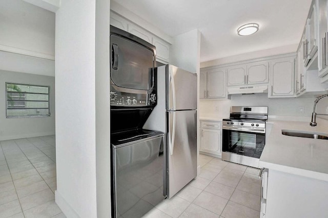 kitchen with sink, white cabinetry, stainless steel appliances, stacked washer / drying machine, and light tile patterned floors