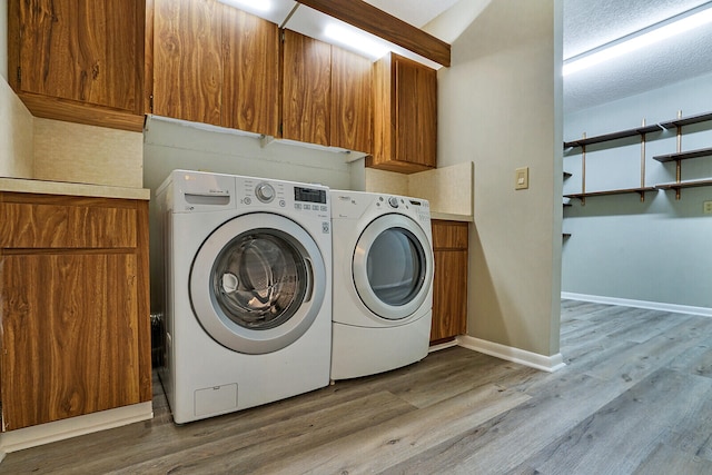 clothes washing area featuring light hardwood / wood-style flooring, washer and clothes dryer, and cabinets