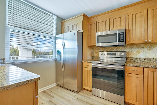 kitchen with light hardwood / wood-style floors, stainless steel appliances, light stone counters, and backsplash