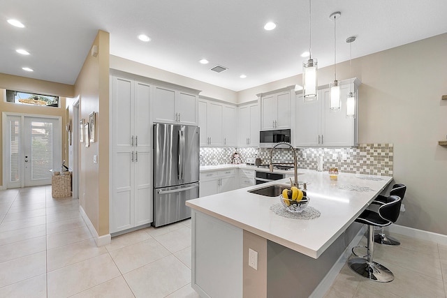 kitchen featuring a breakfast bar area, kitchen peninsula, pendant lighting, white cabinets, and stainless steel refrigerator