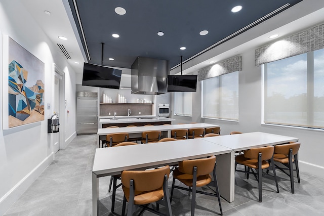 kitchen with wall chimney exhaust hood, stainless steel appliances, a large island, sink, and a kitchen bar