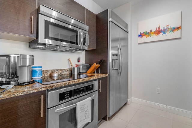 kitchen featuring appliances with stainless steel finishes, dark brown cabinetry, light tile patterned flooring, and dark stone counters