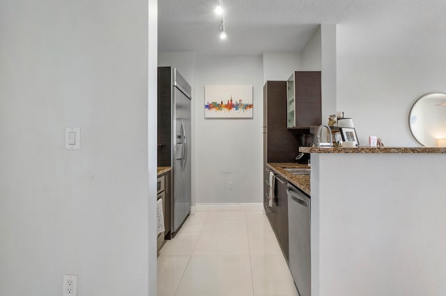 kitchen with stainless steel appliances, dark stone counters, sink, light tile patterned floors, and a textured ceiling