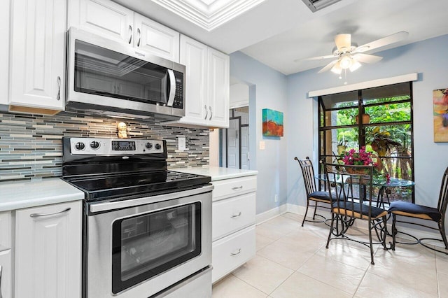 kitchen with appliances with stainless steel finishes, light tile patterned floors, ceiling fan, decorative backsplash, and white cabinetry