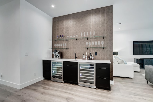 bar featuring light hardwood / wood-style floors, sink, and beverage cooler