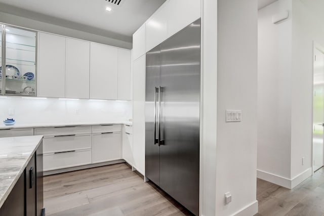 kitchen with light hardwood / wood-style floors, white cabinetry, light stone countertops, and built in fridge